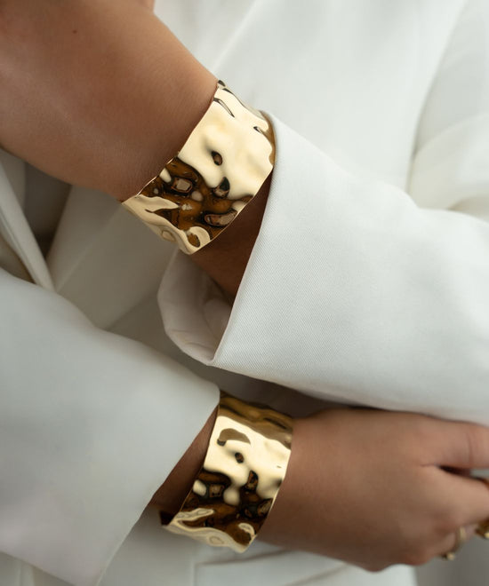Woman wearing the bold Noem bangles in gold from Avelore with a crisp white suit.