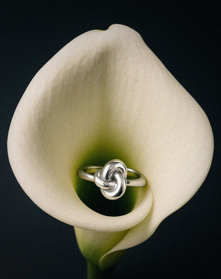 Silver knot Veda ring from Avelore on a white calla lily against a black background