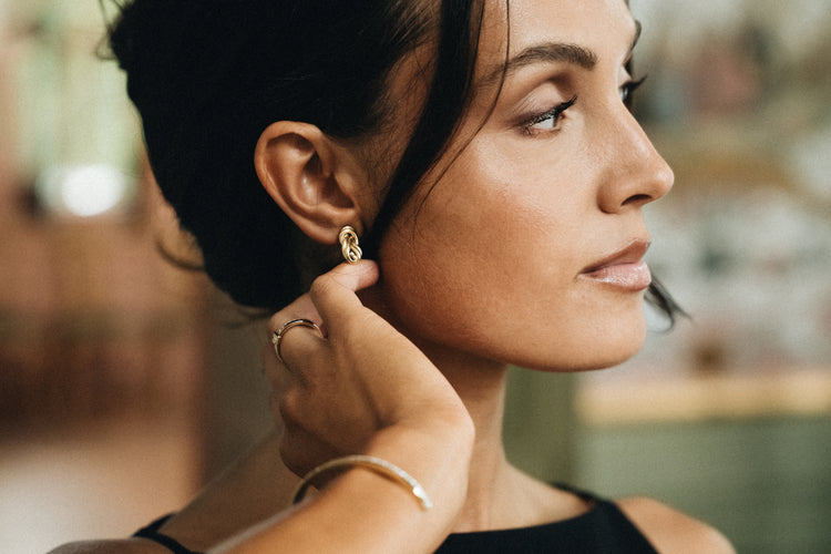 Close-up of a woman adjusting her Naïa Earring from Avelore with a blurred background