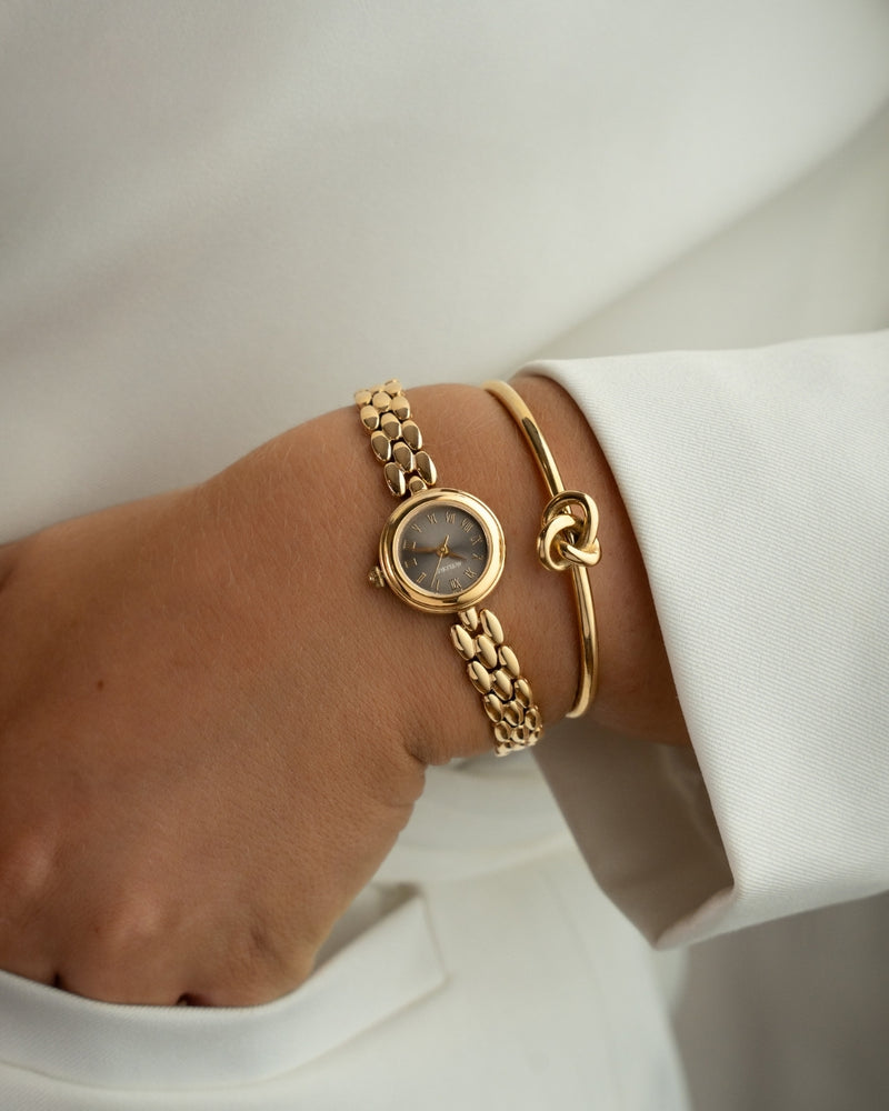 Gold round small watch for women with brown dial and gold band. The model is Eira by Avelore.