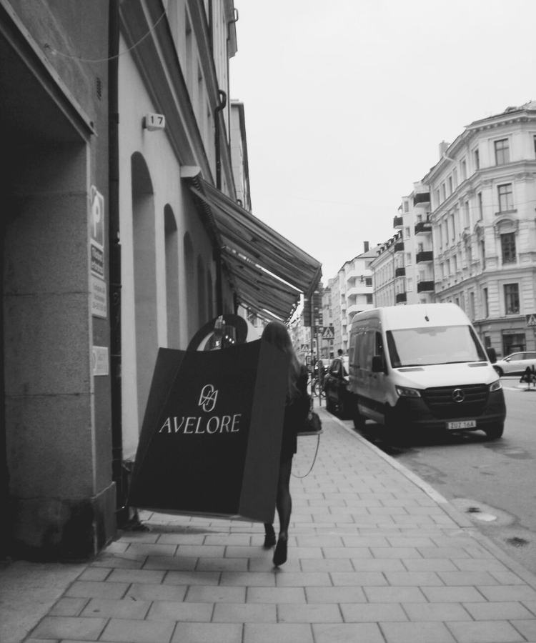 Person walking with an oversized shopping bag with 'Avelore' logo on a city street.
