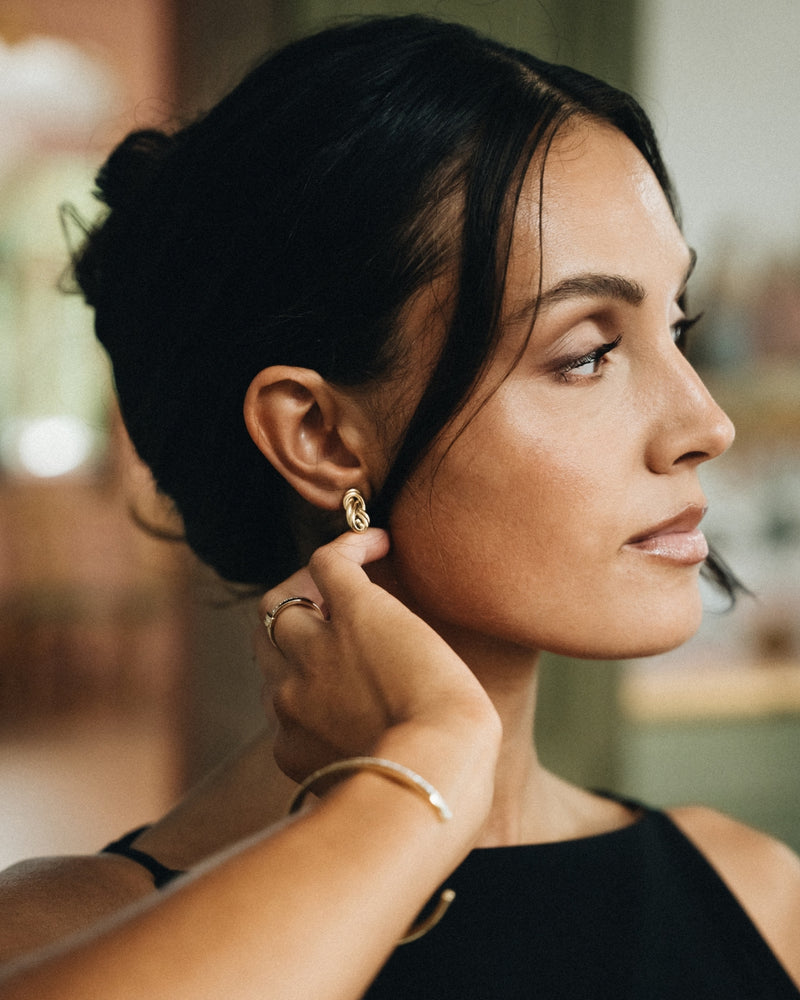 Pair of gold knot earrings. The model is Naia Earrings by Avelore. Women's earrings.