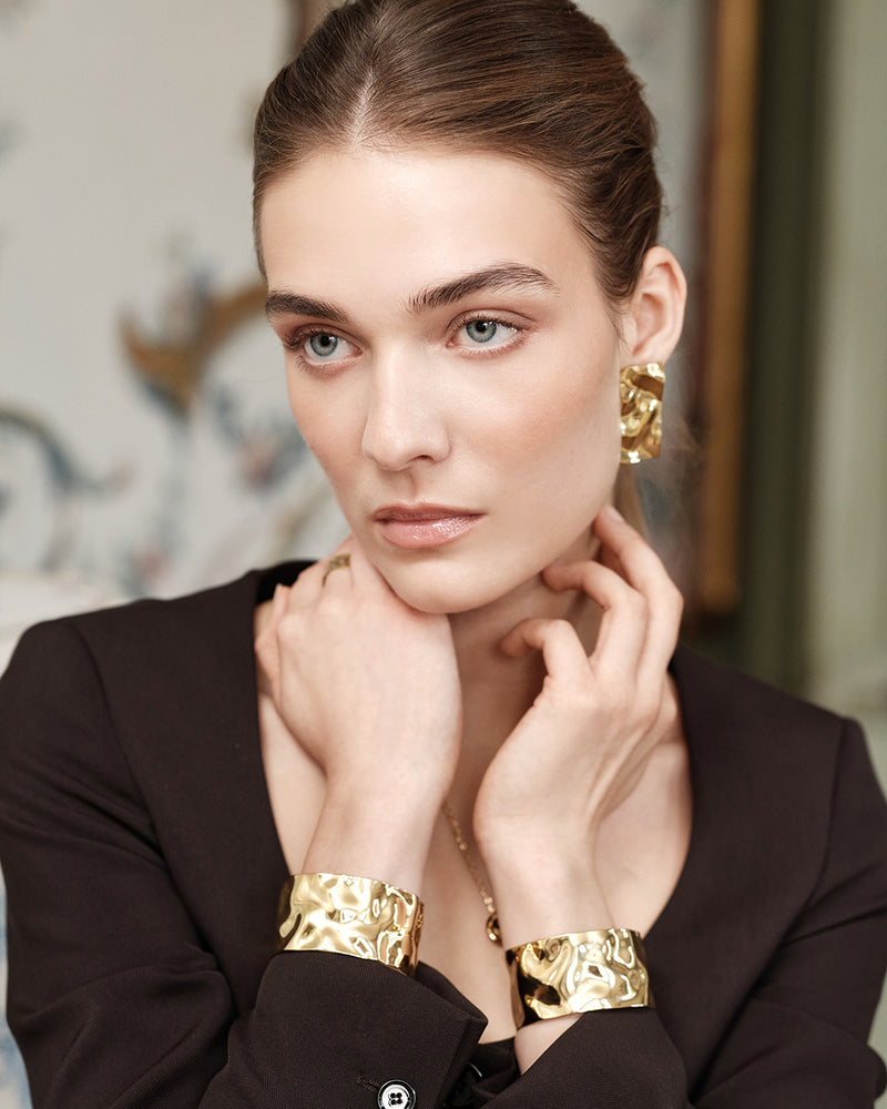Wide gold cuff bracelet with hammered patterned surface. The model is Noem Bangle by Avelore  Women's Bracelets