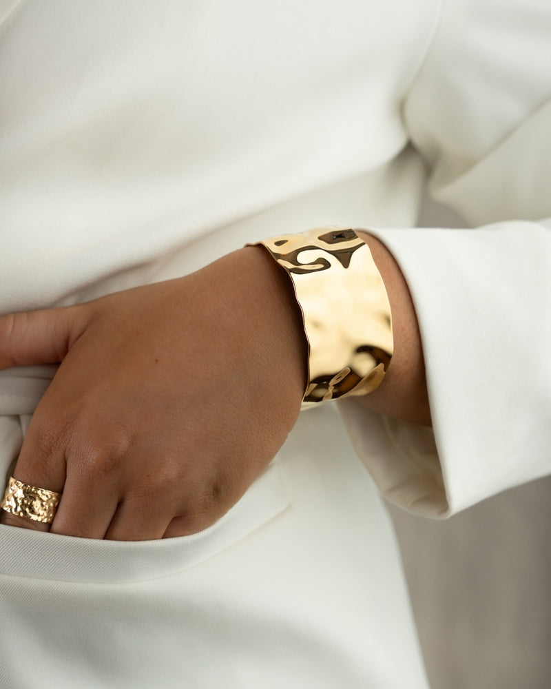 Wide gold cuff bracelet with hammered patterned surface. The model is Noem Bangle by Avelore  Women's Bracelets